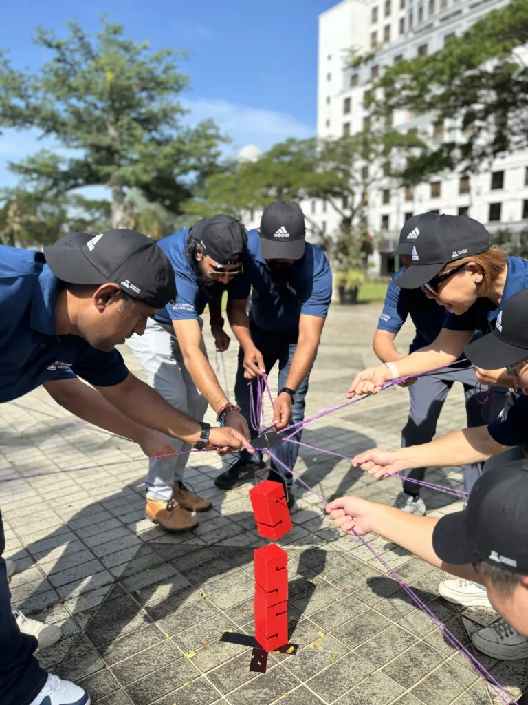 Employees in blue shirts collaborating on a communication and teamwork exercise using purple ropes outdoors, emphasizing real-world problem-solving."